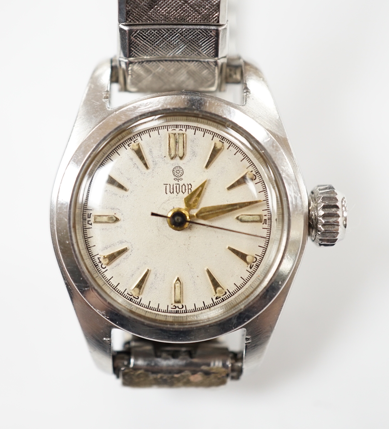 A lady's stainless steel Tudor manual wind wrist watch, with baton numerals, on an associated flexible bracelet.